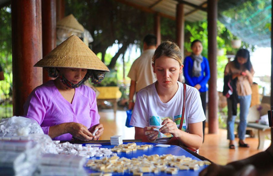 Kampá Tour tourists are experiencing making coconut candy in Ben Tre