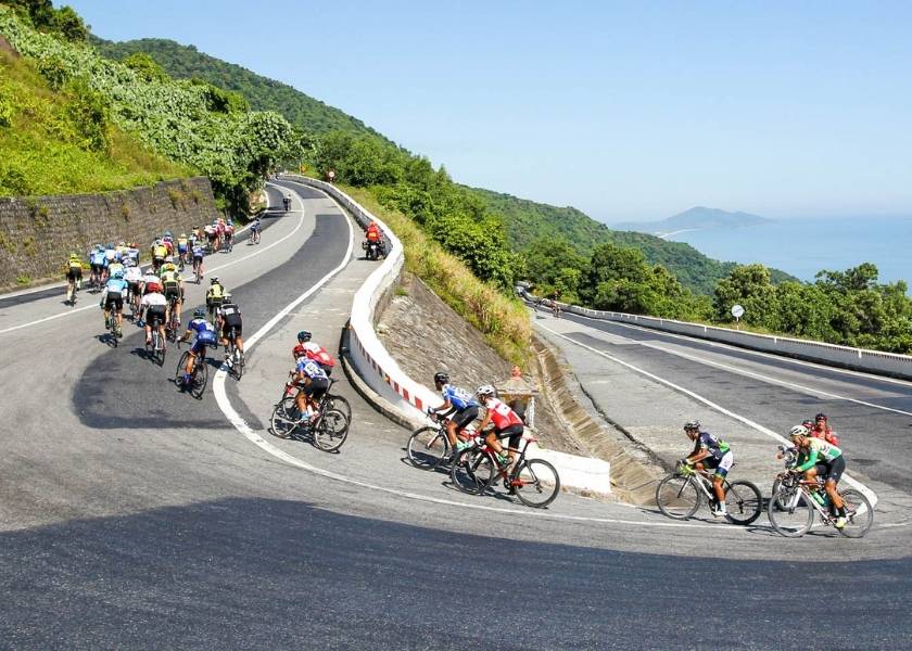 Cyclist standing at the top of Hai Van Pass looking down at the winding coastal road and blue ocean.