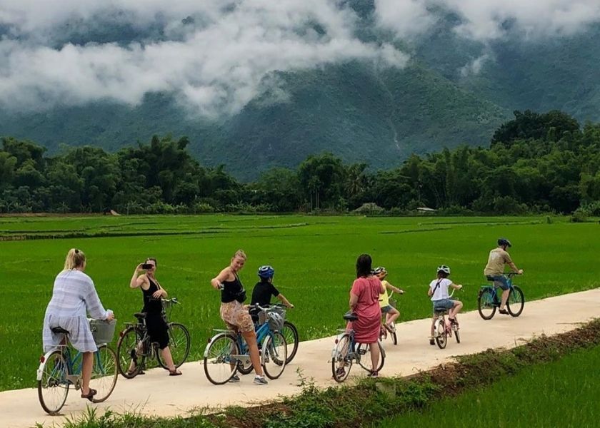 Cyclists riding through green rice paddies and stilt houses in Mai Chau valley, Vietnam.