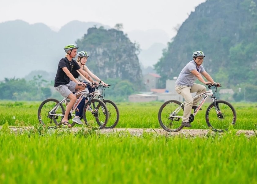 Cycling on a quiet backroad in Tam Coc Ninh Binh next to towering limestone karst mountains.