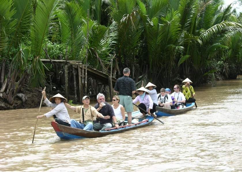Western tourists in traditional wooden sampan boats in Ben Tre, Vietnam.