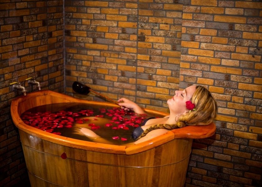 A Western woman relaxes in a traditional Red Dao herbal bath in a wooden tub with rose petals in Sapa, Vietnam.